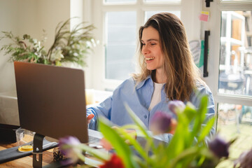 Beautiful young  woman working using computer laptop concentrated and smiling, she sitting at home, freelancer, girl have video call conference. Woman wear blue shirt, look happy.