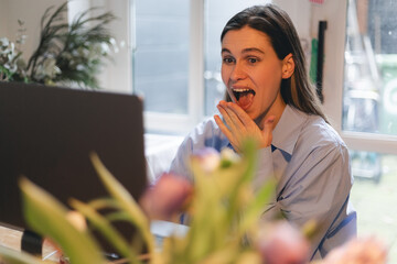 Woman smiles, young hipster working on a laptop at home, writing a message to friends, win in lottery, have a good news, make win gesture and screaming. Happy business woman freelancer.