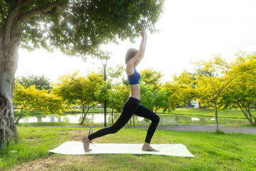 Fototapeta premium Young asian woman in sportswear stretching on a gym mat with a water bottle in a park, doing yoga. The young woman is taking care of her physical and mental health, wellbeing concept.