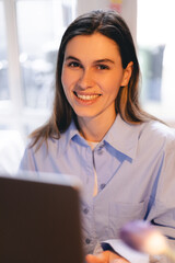 Smiling young woman sit at desk work on laptop or watching webinar, happy girl feel excited browsing internet on computer, using wireless home connection. Technology concept, girl wear blue shirt.