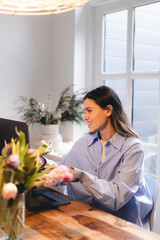 Smiling young woman sit at desk work on laptop or watching webinar, happy girl feel excited browsing internet on computer, using wireless home connection. Technology concept, girl wear blue shirt.