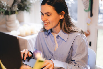 Smiling young woman sit at desk work on laptop or watching webinar, happy girl feel excited browsing internet on computer, using wireless home connection. Technology concept, girl wear blue shirt.