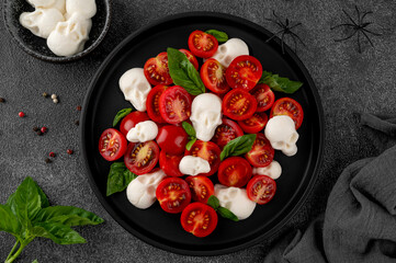 Halloween food. Caprese salad with mozzarella cheese skulls, basil and balsamic dressing on a black plate on a dark background. Funny food idea.