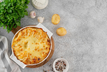 Potato gratin with cream, cheese and garlic in a white ceramic form on a gray concrete background....