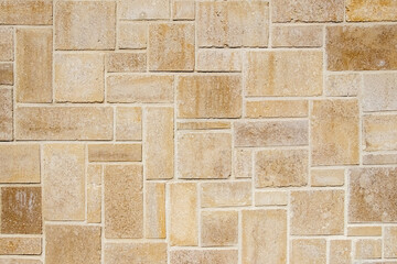 Natural stone masonry with bricks of various sizes and shapes creating a decorative and textured background with a unique, natural pattern and organic shades