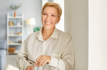 Smiling pleasant middle aged mature happy woman portrait, looking at camera, old attractive beautiful lady posing at home indoor, positive single senior, retired female standing in living room