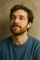 Fototapeta premium Pensive bearded man gazing upward with subtle smile, casual blue sweater against warm textured backdrop, hopeful contemplation, generative AI