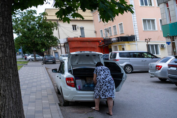 Woman organizes belongings in the trunk of a white car on a busy urban street in the afternoon
