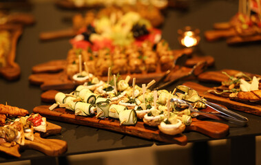 Beautiful fruit platter and assorted finger foods arranged on wooden boards in warm indoor lighting, creating a cozy and elegant catering display with candlelight ambiance.