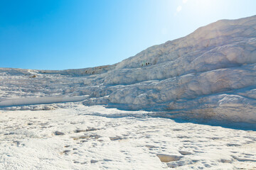 Natural calcium-rich travertine formations in Pamukkale, Türkiye, illuminated by bright sunlight. Unique white landscape formed by thermal spring waters flowing over terraced limestone surface