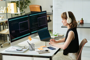 Caucasian young adult woman wearing headphones developing neural network code on desktop computer...