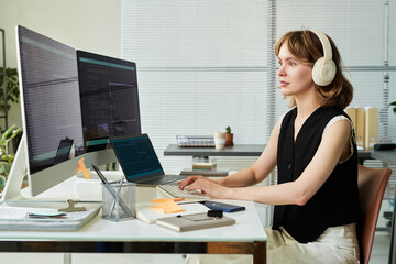 Caucasian young adult woman wearing headphones working on neural network development at desk using...