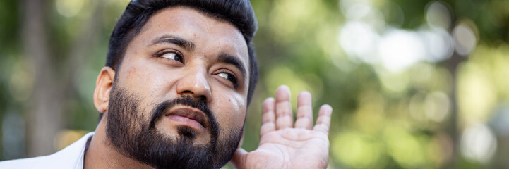 Curious and questioning young South Asian Indian man listening to bad news with negative expression, concept image for ear care, hard of hearing, fake news, rumors