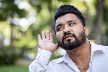 Curious and questioning young South Asian Indian man listening to bad news with negative expression, concept image for ear care, hard of hearing, fake news, rumors