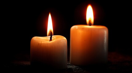 two burning candles in the dark .