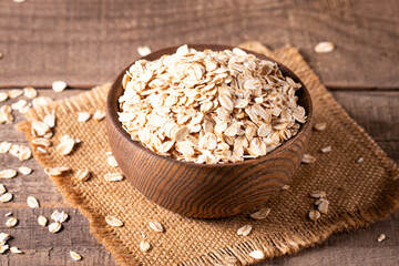 Raw oats in a wooden bowl on a wooden background. Organic food concept. 