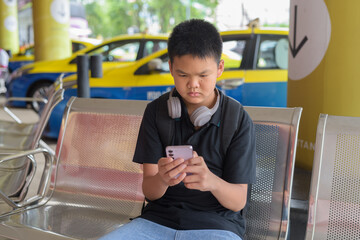 Thai teen boy wearing headphones using phone with city taxis in background