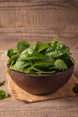 Green baby spinach leaves in wooden bowl on wooden background. Organic food concept. 