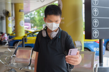 Thai boy with facial mask with taxis in background wearing headphones