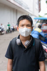 Thai boy with facial mask with tuk tuk taxis in background wearing headphones