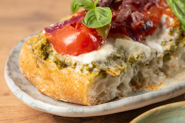 Close up of a toasted slice of bread topped with pesto, fresh tomatoes, melted mozzarella, and caramelized red onions, creating a vibrant and appetizing bruschetta