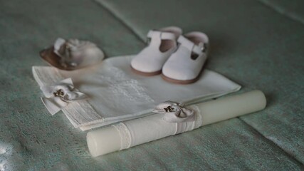 christening set with baby shoes candle embroidered cloth and bonnet arranged on soft fabric