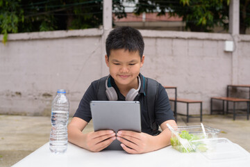 Thai boy eating salad and using wireless technology at outdoor table