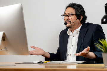 Happy office employee wearing headphones, enjoying a virtual meeting at his modern workstation.