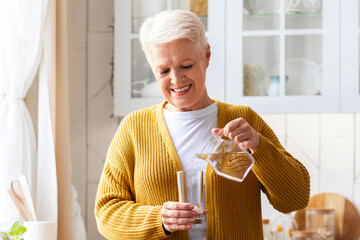 Hydration, healthy lifestyle cocnept. Smiling senior woman pouring water into glass, kitchen...