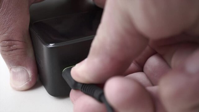 Close-up footage of a male hand connecting a USB cable to a portable power bank. Captures the concept of mobile energy, battery charging, and on-the-go technology. Ideal for illustrating tech tutorial