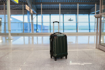 A suitcase stands alone on the floor in an airport terminal, symbolizing travel and waiting.