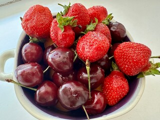 Fresh strawberries and juicy cherries in a ceramic bowl on a white background. Summer berries with...