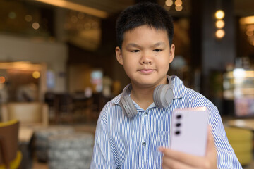 Thai boy using phone at cafe with headphones