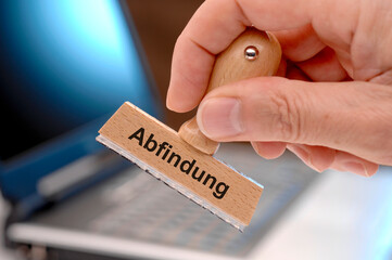 Ein Holzstempel ist beschriftet mit dem Aufdruck Abfindung