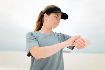 Runner adjusts her smartwatch while preparing for a workout under a cloudy sky at the beach