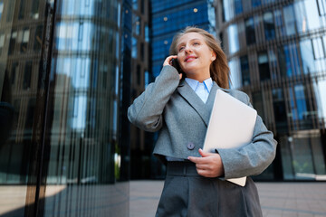 Busy professional enjoys a sunny day while discussing business on the phone near modern high-rise...