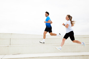 Couple enjoying a lively run together on elegant white steps under a bright sky in the morning sun,...