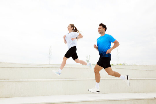 Dynamic couple running through outdoor steps in bright athletic gear during a cloudy day in a lively urban park