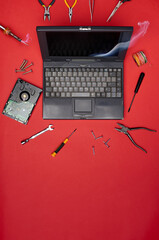 Old laptop surrounded by tools and electronic parts on red background. Concept of computer repair, vintage tech maintenance, and DIY electronics
