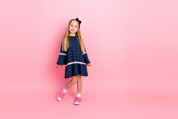 Adorable young girl in stylish casual dress posing confidently against a pink background with...