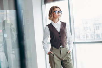 Successful businesswoman in formal attire standing in a bright office with large windows exuding professionalism and style