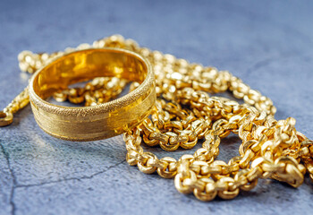 Gold price, gold jewelry, close-up of gold ring and gold necklace on grey background.