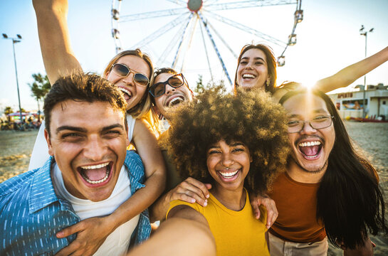 Multiracial group of friends taking selfie with smart mobile phone outside - Happy young people having fun in front of ferris wheel at summer vacation - Technology and summertime holidays concept - Powered by Adobe