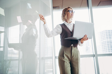 Confident businesswoman presenting ideas in a modern office holding a laptop in a bright workspace