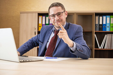 Professional man gesturing confidently while seated at desk with laptop in modern office setting