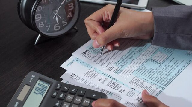checking tax forms and using a calculator and pen filling US 1040 tax form Making financial report