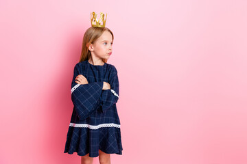Adorable young girl with a crown posing confidently against a vibrant pink background in a stylish dress