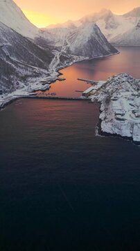 Hus&oslash;y auf Senja in Norwegen im Schneesturm, arktische K&uuml;stensiedlung unter orange gef&auml;rbtem Himmel bei dichtem Schneefall und winterlichen Bedingungen im Nordmeer