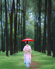 Traditional Japanese Woman in Furisode Kimono with red wagasa umbrella in Pine Forest. Cultural fashion and nature harmony.