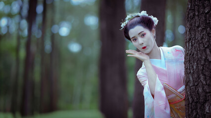 Traditional Japanese Woman in pink Furisode Kimono in a peaceful natural green pine forest....